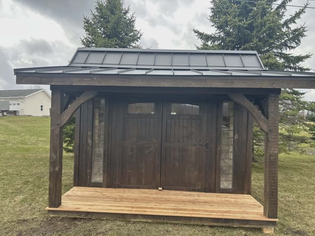 Front exterior view of a dark brown garden shed with covered porch and metal roof