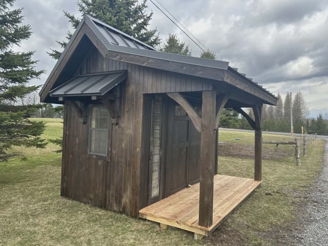 Angled exterior view of a dark brown she shed with front porch and pitched metal roof
