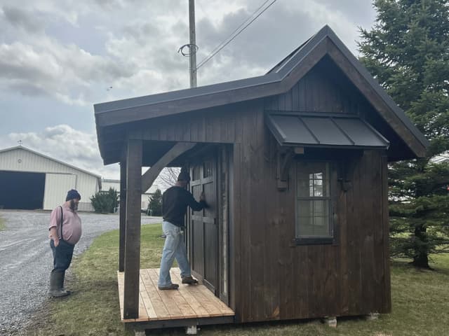 Side front view of a dark brown garden shed with covered entry and metal roof